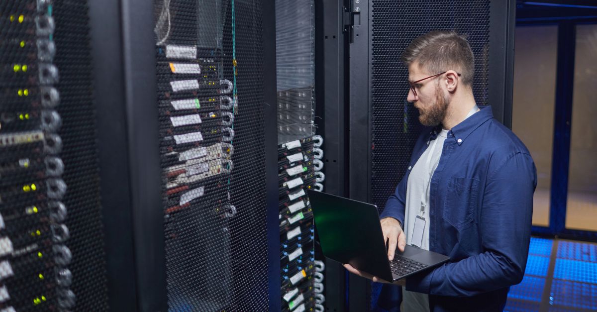 Inżynier IT sprawdzający konfigurację serwerów rack w centrum danych z laptopem – analiza parametrów wydajności, TCO i zgodności ze strategią HA firmy.